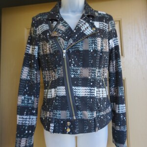 May include: A patterned jacket with a black, white, and blue plaid design. The jacket features a diagonal zipper, two front pockets, and gold-colored buttons. The jacket is displayed on a white mannequin.