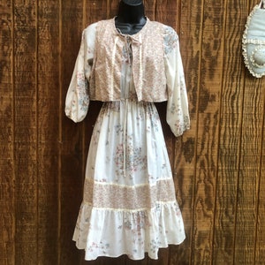 May include: A white dress with a floral print and a matching brown vest. The dress has a cinched waist and a tiered skirt.