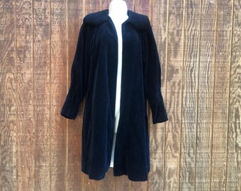 May include: A long, dark navy blue velvet coat with a wide collar. The coat is open in the front, revealing a white garment underneath. The sleeves are long and the coat reaches to mid-calf length. The coat is displayed on a mannequin.