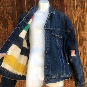 May include: A vintage denim jacket with a colorful striped lining. The jacket is a medium wash blue with button closures and a Levi's patch on the sleeve. The lining features stripes of yellow, green, white, and navy.