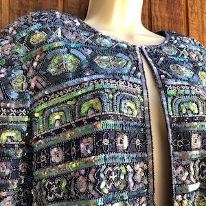 May include: A blue sequined jacket with a geometric pattern. The jacket has a front closure and long sleeves.