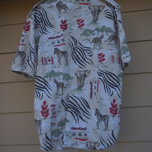 May include: Short-sleeved button-down shirt with an all-over safari animal print. The cream-colored shirt features zebras, elephants, cheetahs, and lions, with red and green accents. Black zebra stripes are also incorporated into the design.