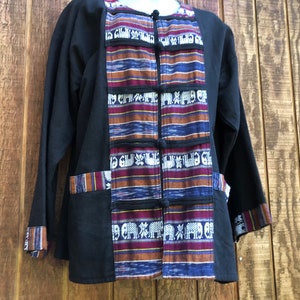 Puede incluir: Una chaqueta negra con un panel frontal estampado. El panel presenta un diseño repetitivo de elefantes, flores y formas geométricas en tonos marrones, azules, morados y blancos.