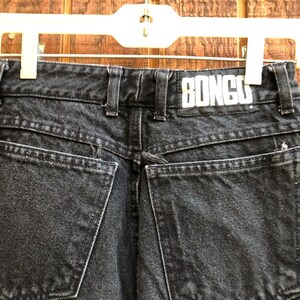 May include: Close-up of the back of black denim jeans with the brand name "BONGO" on the waistband. The jeans have two back pockets and a classic five-pocket design. The denim has a faded, worn look.
