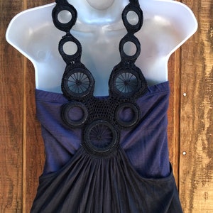 Op de afbeelding: Een marineblauwe jurk op een witte mannequin. De jurk heeft een haltertop met een decoratief zwart gehaakt ontwerp en een zwierige rok. De achtergrond is een houten oppervlak.
