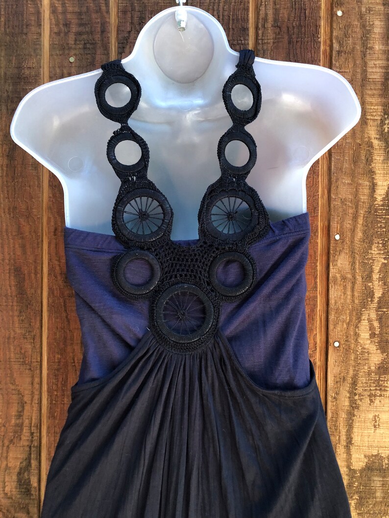Op de afbeelding: Een marineblauwe jurk op een witte mannequin. De jurk heeft een haltertop met een decoratief zwart gehaakt ontwerp en een zwierige rok. De achtergrond is een houten oppervlak.