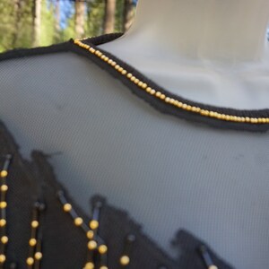 Pode incluir: Top preto de malha com detalhes de contas douradas em torno do decote.