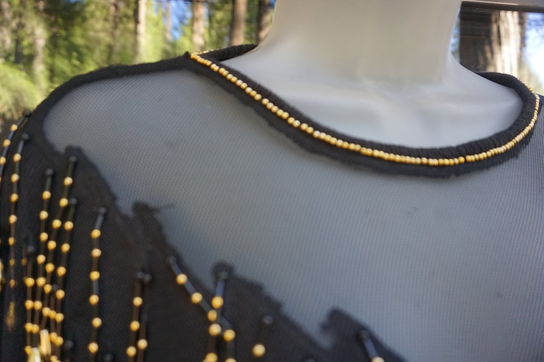 Pode incluir: Top preto de malha com detalhes de contas douradas em torno do decote.