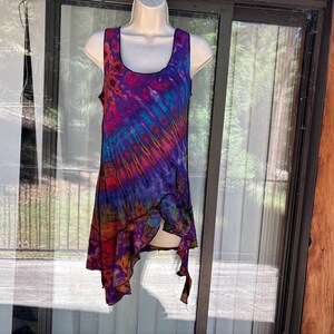 May include: A sleeveless tank top featuring a vibrant tie-dye pattern in shades of purple, blue, red, and orange. The garment has a scoop neckline and an asymmetrical hemline with a black stitched edge, displayed on a white mannequin torso.