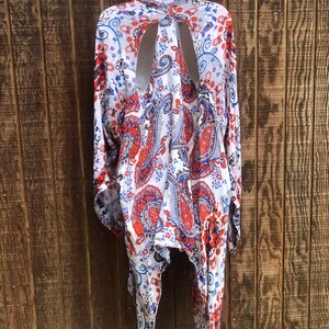 May include: A white, red, and blue paisley print kimono-style top with long sleeves and a unique open back design. The lightweight fabric hangs from a hanger against a wooden background.