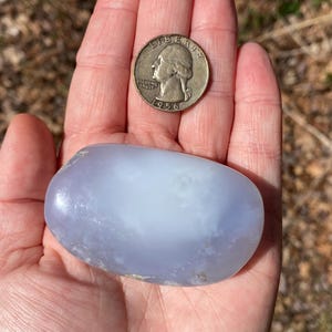 May include: A smooth, light blue agate stone with a white center, about the size of a US quarter.