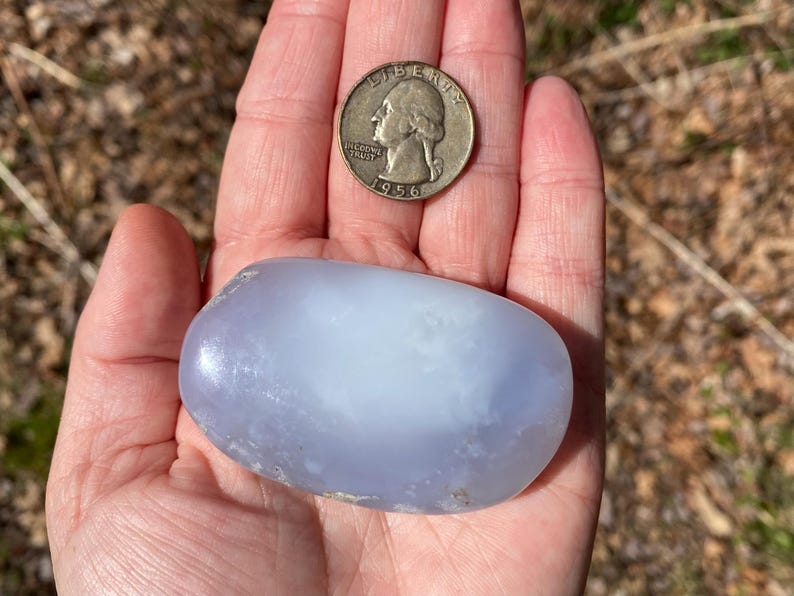 May include: A smooth, light blue agate stone with a white center, about the size of a US quarter.