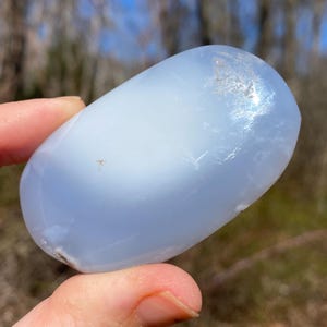 May include: A smooth, light blue, oval-shaped, polished stone. The stone has a cloudy, translucent appearance.