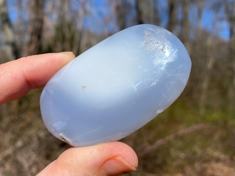 May include: A smooth, light blue, oval-shaped, polished stone. The stone has a cloudy, translucent appearance.