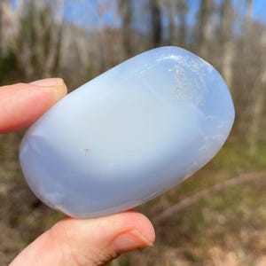 May include: A smooth, light blue and white agate stone with a rounded, oval shape.