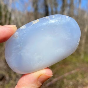 May include: A smooth, light blue, oval-shaped, polished stone with white inclusions.