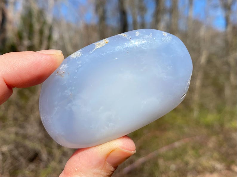 May include: A smooth, light blue, oval-shaped, polished stone with white inclusions.