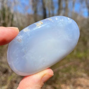 May include: A smooth, light blue, oval-shaped, polished blue lace agate stone with white and gray inclusions.