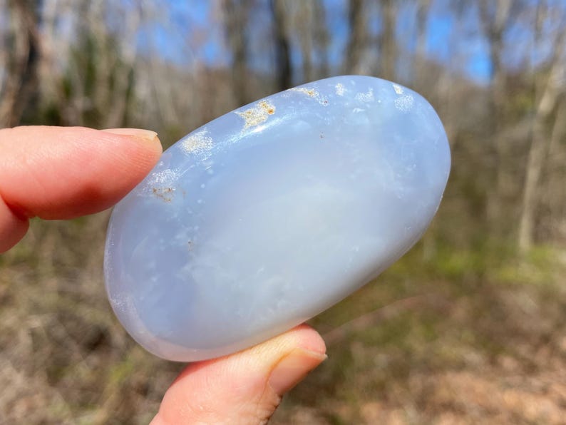 May include: A smooth, light blue, oval-shaped, polished blue lace agate stone with white and gray inclusions.