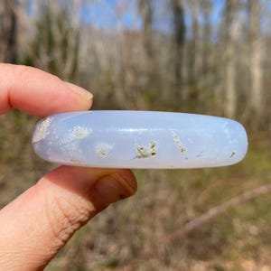 May include: A light blue agate stone with white and brown inclusions. The stone is smooth and polished, and it is being held in a hand.