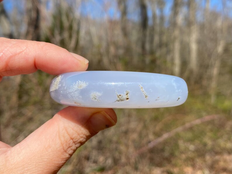 May include: A light blue agate stone with white and brown inclusions. The stone is smooth and polished, and it is being held in a hand.
