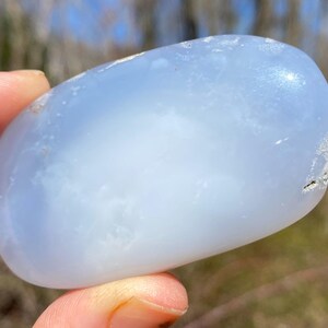 May include: A smooth, light blue, oval-shaped chalcedony stone with a cloudy, translucent appearance.