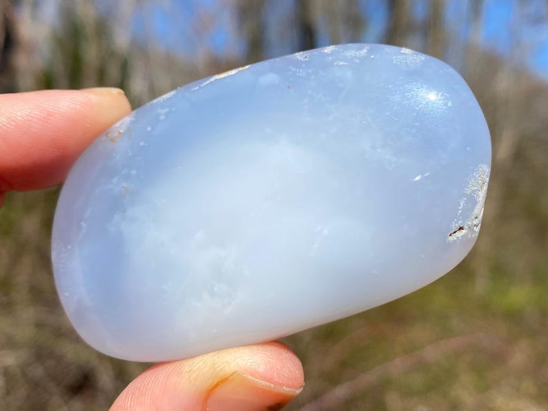 May include: A smooth, light blue, oval-shaped chalcedony stone with a cloudy, translucent appearance.