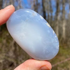 May include: A smooth, light blue and white agate stone, polished to a smooth finish. The stone has a cloudy, translucent appearance with white swirls and patterns.