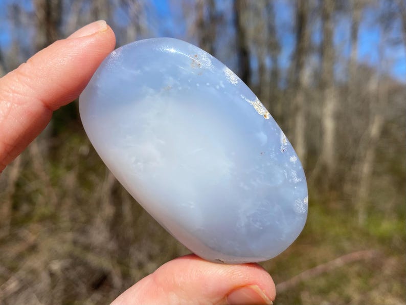 May include: A smooth, light blue and white agate stone, polished to a smooth finish. The stone has a cloudy, translucent appearance with white swirls and patterns.