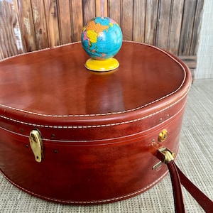 May include: A vintage, reddish-brown suitcase with white stitching and brass hardware. A small, colorful globe sits atop the suitcase. The suitcase has a handle and a clasp closure, suggesting travel and exploration.
