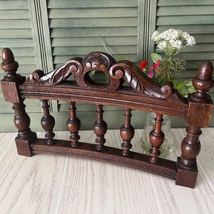 May include: A dark brown wooden decorative railing featuring a curved top rail with carved scrollwork and a central shell motif. The structure includes five vertical turned spindles and two square end posts topped with acorn-shaped finials.