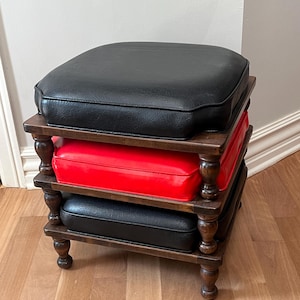 May include: A three-tiered wooden stool with a dark finish. The top and bottom tiers feature black, square cushions, while the middle tier has a red cushion. The stool has turned legs and a classic design.