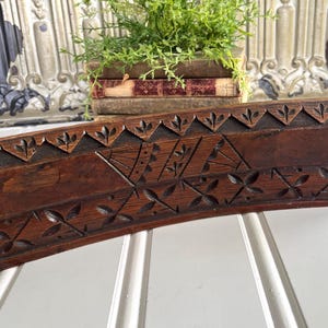 May include: A dark brown wooden architectural molding piece featuring hand-carved geometric patterns. The top edge displays a repeating triangular motif with floral accents, while the lower section includes a series of carved leaf-like shapes.