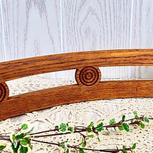 May include: A curved, wooden shelf with a warm, brown finish. The shelf features decorative, carved spiral designs on each end and in the center. The shelf is approximately 12 inches long and is designed to hold items.