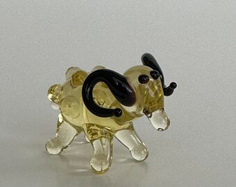 May include: A small glass figurine of a ram with yellow glass body and black glass horns. The ram has a detailed face with black eyes and a small mouth.