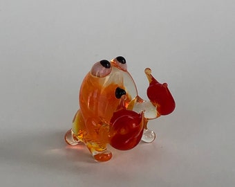 May include: A small, translucent glass figurine of a crab. The creature is crafted from orange and yellow glass with distinct red claws and black eyes. It is depicted in a standing position with its claws raised, showcasing smooth, glossy surfaces.