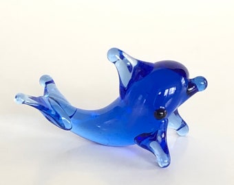 May include: A small blue glass dolphin figurine. The dolphin is in a swimming pose with its tail and fins outstretched.