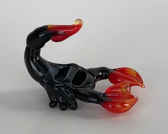 May include: A black glass scorpion figurine with red and orange accents. The scorpion is curled up in a defensive position with its tail raised.
