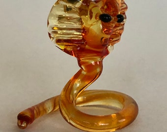 May include: A small glass sculpture of a coiled amber-colored snake with black eyes. The snake's head is raised and has a textured, detailed design.