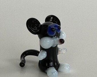 May include: A black glass mouse figurine with white accents and blue eyes. The mouse is sitting up with its tail curled behind it.