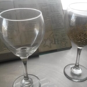 May include: Two clear glass wine glasses, one with a gold glitter design on the inside.
