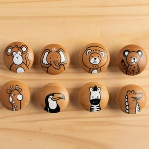 Könnte beinhalten: Acht Holzgriffe mit verschiedenen Tierillustrationen, die darauf gemalt sind. Die Tiere sind ein Affe, ein Elefant, ein Löwe, ein Leopard, eine Giraffe, ein Tukan, ein Zebra und ein Krokodil.