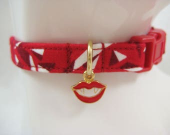 May include: Red and white patterned cat collar with a gold-colored charm of vampire lips. The collar has a red plastic buckle and is displayed on a white mannequin head. The collar is approximately 0.5 inches wide.