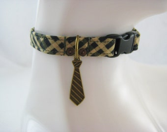 May include: A patterned dog collar with a black plastic buckle. The collar is tan and green with a plaid design. A bronze-colored tie charm hangs from the collar.