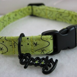 May include: A lime green pet collar with a black plastic buckle and a black metal charm that says "Spooky". The collar has a repeating pattern of black stars and swirls.