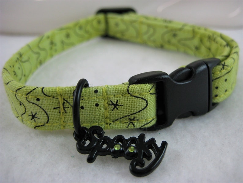 May include: A lime green pet collar with a black plastic buckle and a black metal charm that says "Spooky". The collar has a repeating pattern of black stars and swirls.