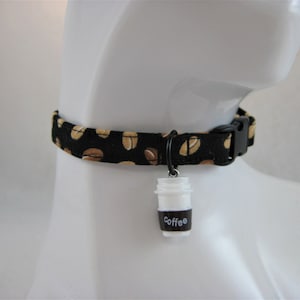 Könnte beinhalten: Schwarzes Hundehalsband mit Kaffeebohnenmuster und schwarzer Kunststoffschnalle. Ein kleiner weißer Kaffeebecher-Anhänger mit dem Wort "Coffee" ist am Halsband befestigt.