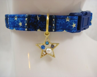 May include: A blue pet collar with a star pattern and a blue plastic buckle. A gold-colored star charm with blue, white, and purple gemstones and a pearl hangs from the collar. The collar is approximately 1 inch wide.