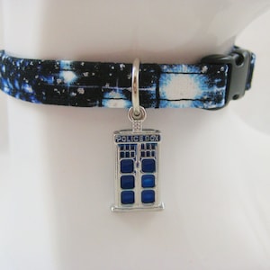 Könnte beinhalten: Hundehalsband mit einem schwarzen und blauen Galaxiemuster. Der silberne Anhänger zeigt eine blaue Police Box mit der Aufschrift "POLICE BOX". Der Kragen hat eine schwarze Kunststoffschnalle.