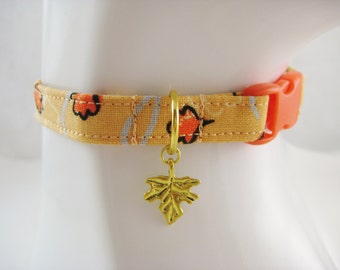 May include: A yellow and orange patterned pet collar with an orange plastic buckle. The collar has a gold leaf charm. The pattern includes orange flowers and gray stripes on a yellow background.